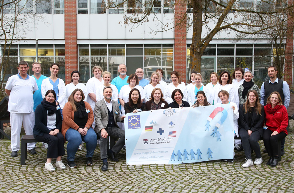 Florrie Vanek, Emma Cotter, Annelies Pfeiffer Wood, hold a Magnet4Europe banner in the center of a group photo with Universitätsklinikum Regensburg employees